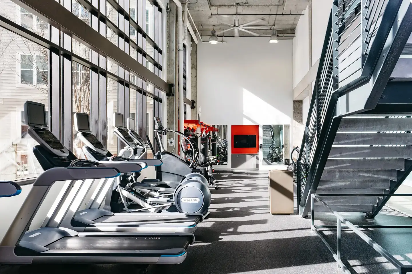 Fitness center with treadmills alongside large open windows and stairs leading to a second floor.